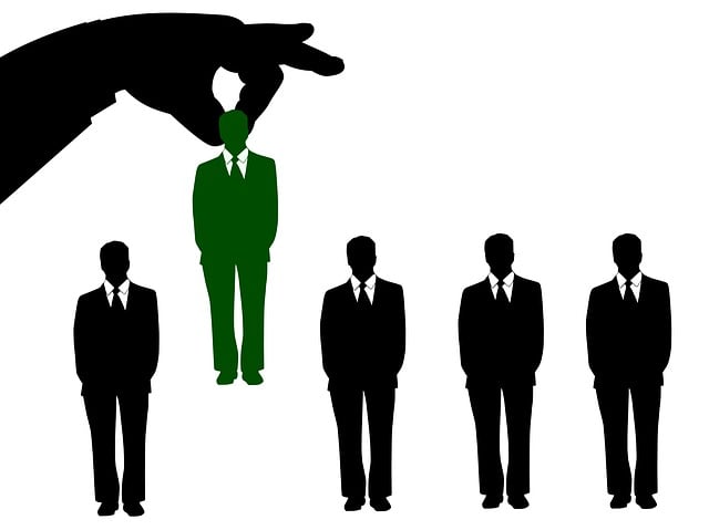 Graphic. A giant hand plucks out a person from a row of identical men in suits.