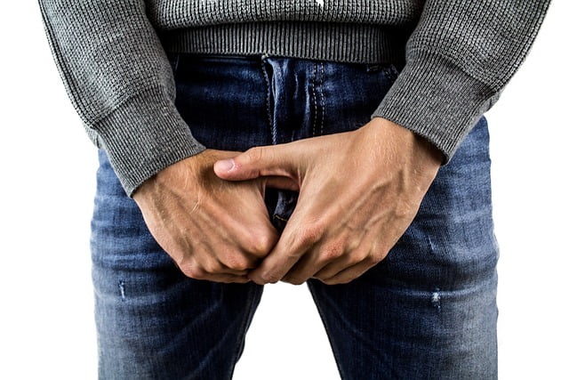 Photo of a man in blue jeans clutching his crotch with both hands.